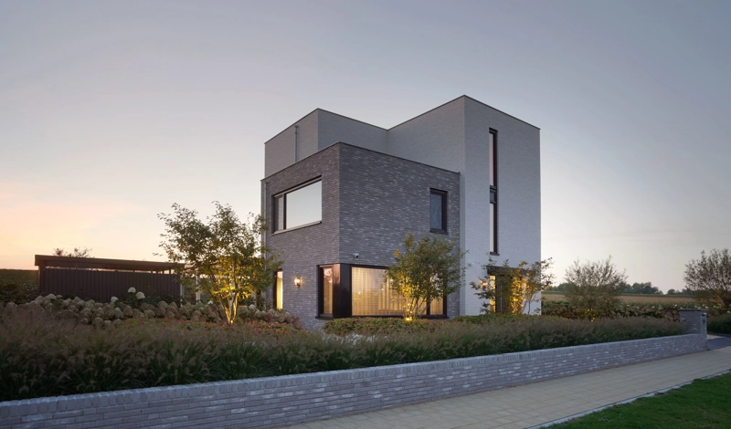 De zijgevel van een moderne, kubistische villa met wit-grijze gevelafwerking